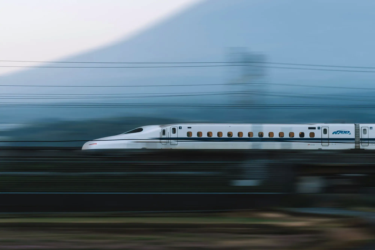 A Japanese Shinkansen bullet train speeding flawlessly past a blurred, faded silhouette of Mount Fuji.