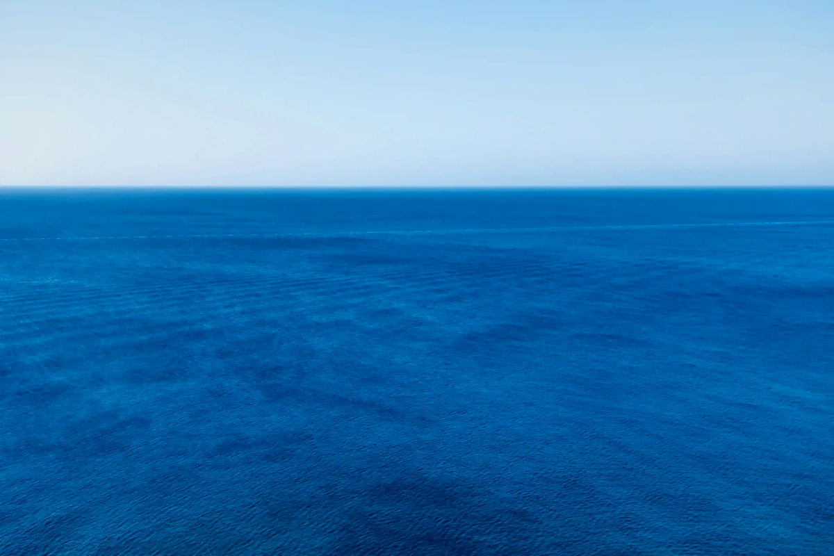 A minimalist and vast deep blue ocean meeting a clear sky at a sharp horizon line, illustrating the calming neurological state of the blue mind.