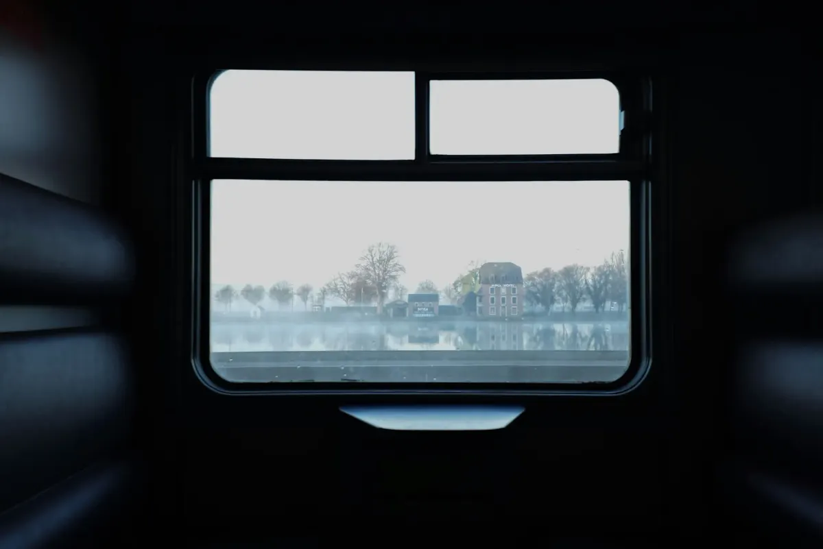 A cinematic, moody view from a dark train window overlooking a misty landscape, representing the mystery travel trend and the death of the itinerary.