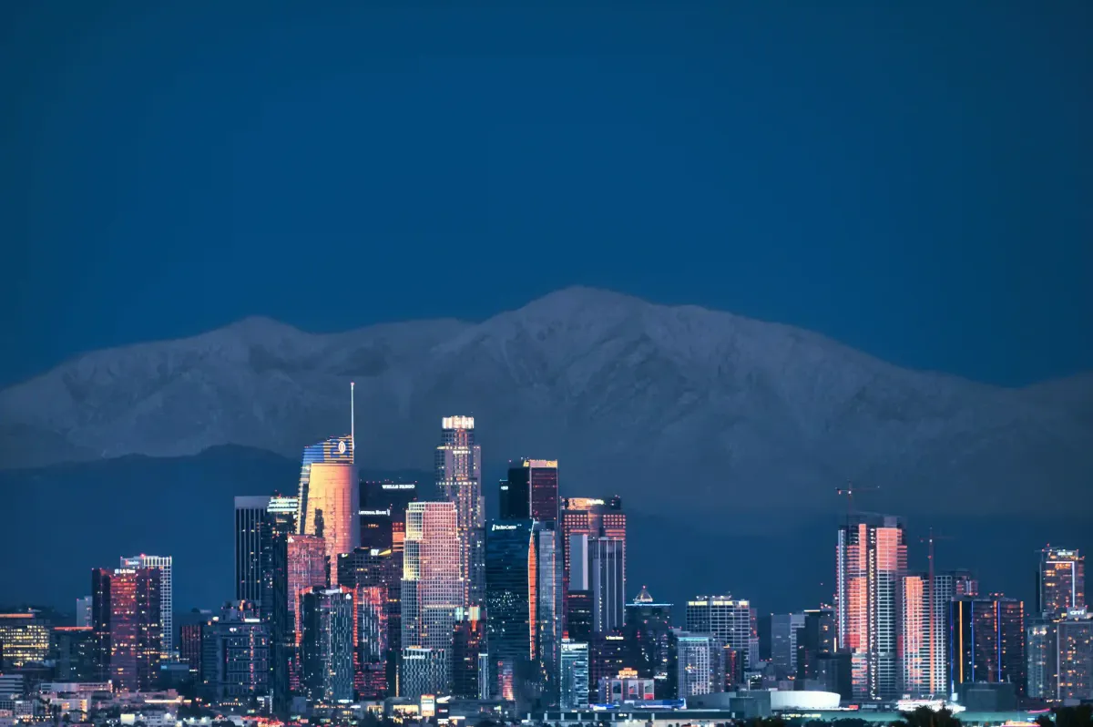 Brightly lit Los Angeles skyline at dusk against a mountain backdrop, illustrating the intense urban light pollution that blocks out the night sky.