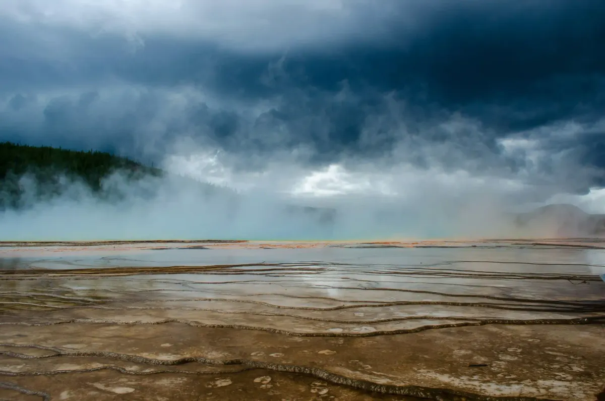 Dark storm clouds gather over the steaming, mineral-rich terraces of Yellowstone, revealing the raw and volatile landscape of the supervolcano.