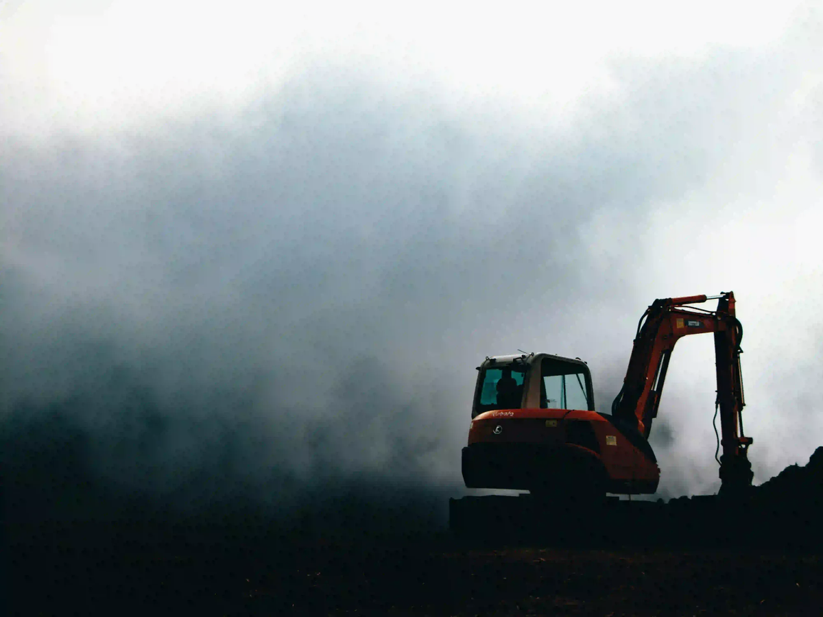 A silhouette of an industrial excavator surrounded by dense, dark mist