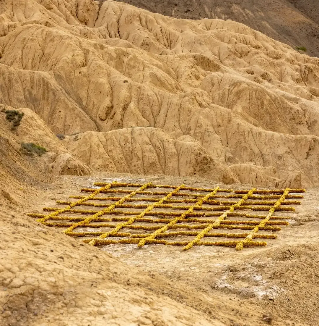 A yellow grid land art installation by Studio Eidola resting on the dry, eroded mountain terrain of Lamayuru for the sa Ladakh Biennale.