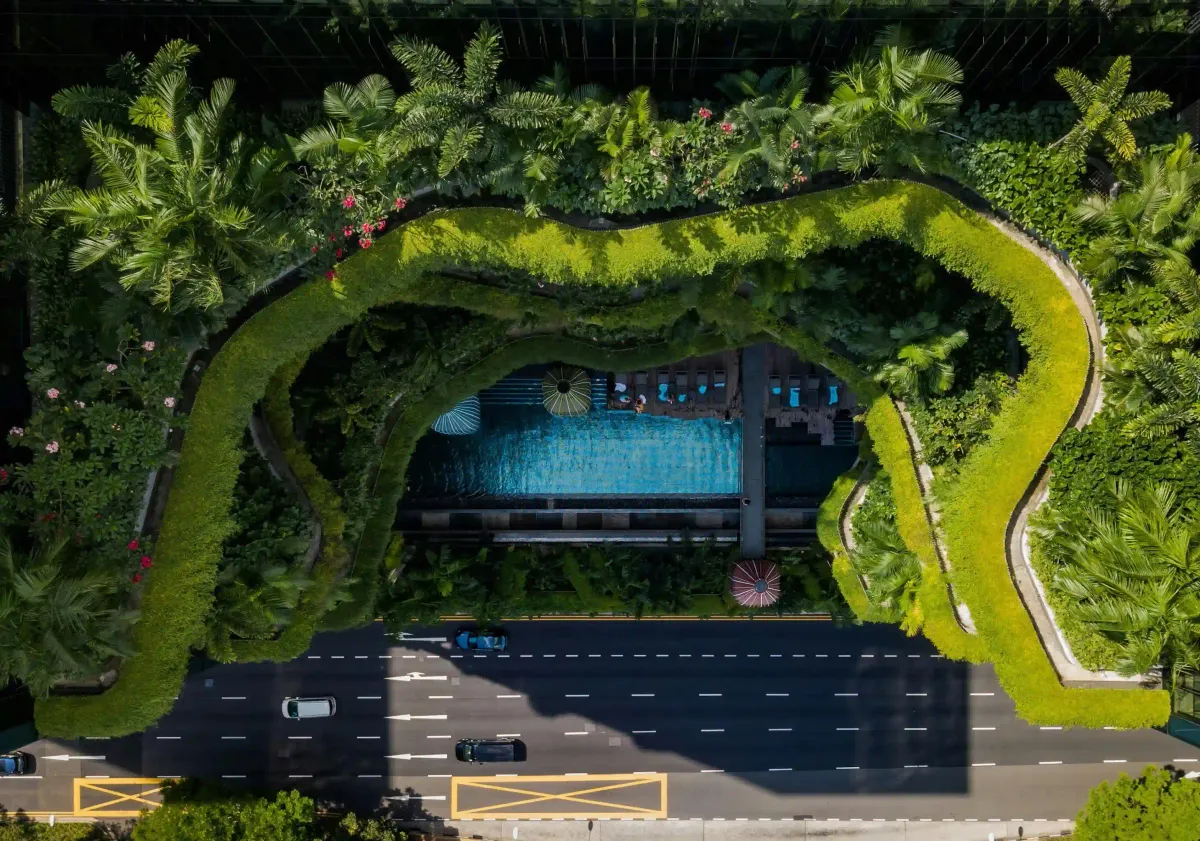 Aerial view of a biophilic building in Singapore with lush green terraces directly contrasting with the adjacent asphalt city road.