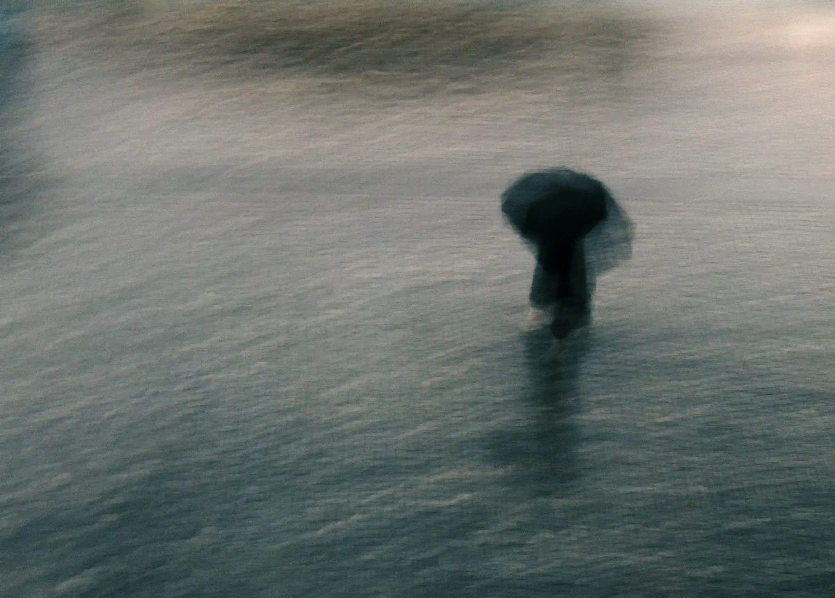 A heavily blurred silhouette of a solitary figure with an umbrella walking in the rain, symbolizing urban isolation and visibility fatigue.