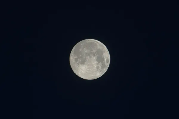 A highly detailed, pale full moon glowing against a pitch-black night sky, revealing its true color rather than a blue hue.