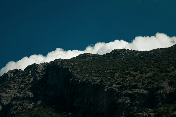 Imposing dark mountain ridge along the Lycian Way, contrasting with bright white clouds and a deep blue sky.