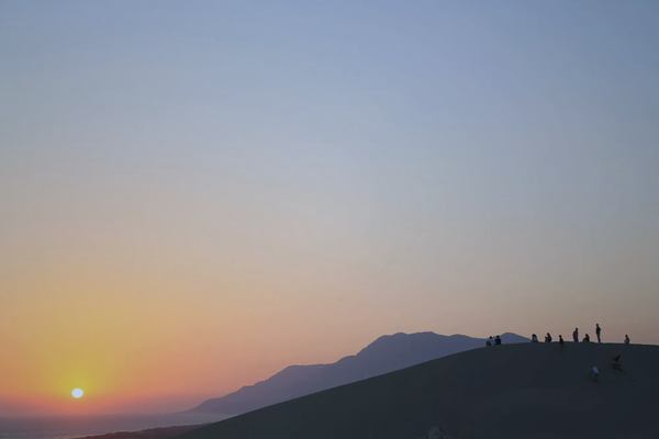 Silhouettes of people sitting on massive sand dunes watching the sunset at Patara, Turkey.