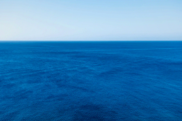 A minimalist and vast deep blue ocean meeting a clear sky at a sharp horizon line, illustrating the calming neurological state of the blue mind.