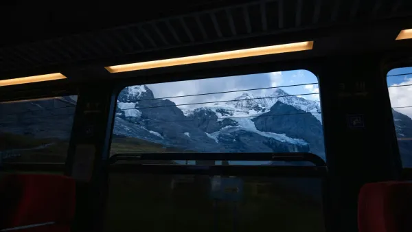 A view from inside a dark train carriage looking through large windows at massive snow-capped mountains, representing scenic slow travel in Europe.