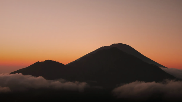 A dark mountain silhouette against an orange sky in Bali, symbolizing the island's imposing new tourism rules and digital borders.