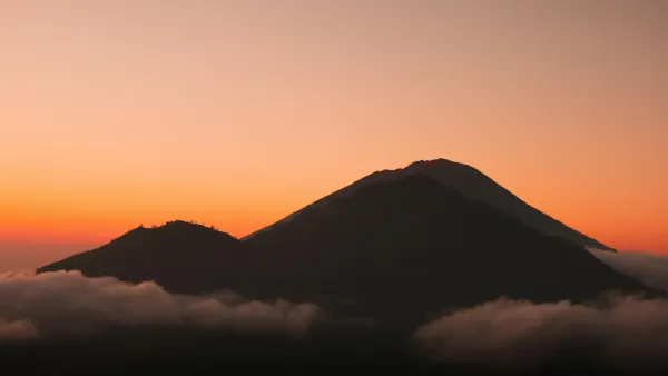 A dark mountain silhouette against an orange sky in Bali, symbolizing the island's imposing new tourism rules and digital borders.