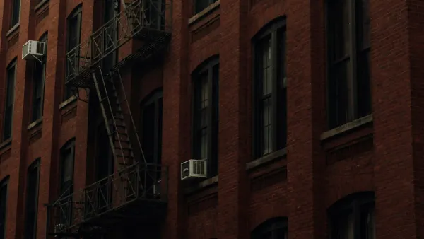 Historic red brick building with iron fire escapes in New York, representing the tangible urban memory against the flawless grid.