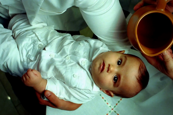 A cinematic still from the documentary Samsara, showing a baby looking directly into the lens during a ritual, representing the profound and fragile human experience on earth.