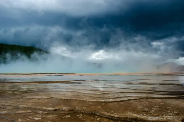 Dark storm clouds gather over the steaming, mineral-rich terraces of Yellowstone, revealing the raw and volatile landscape of the supervolcano.