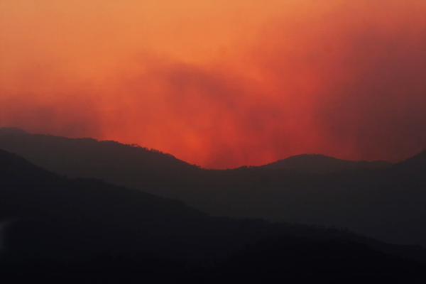 Silhouettes of mountain ridges against a hazy, deep orange and red sky heavily polluted by wildfire smoke.
