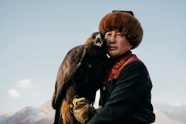 A striking portrait of a traditional Kazakh eagle hunter holding his golden eagle against a moody sky, representing cultures defying global monoculture.