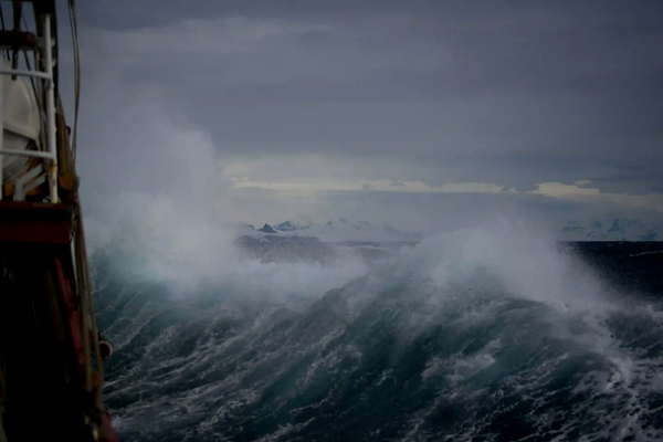 Moody low-exposure photo from a ship's deck showing large, dark, crashing waves on a stormy ocean, evoking the dangerous and desperate setting of World War II naval battles.