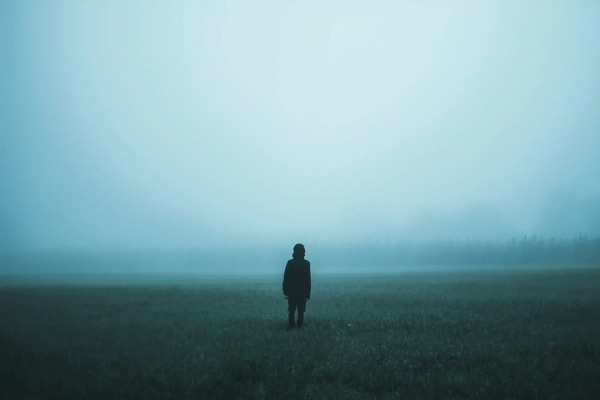 A moody, low-exposure photograph of a lone silhouette standing in a vast, heavy fog, representing unseen mental boundaries and isolation.