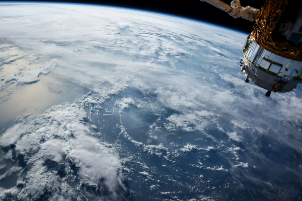 View of Earth's curvature and cloud cover from space with a satellite instrument visible in orbit.