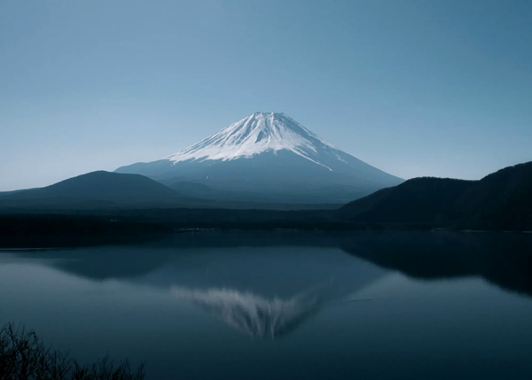 A wide, low-exposure view of Mount Fuji and its perfect reflection on a dark, still lake under a muted sky.