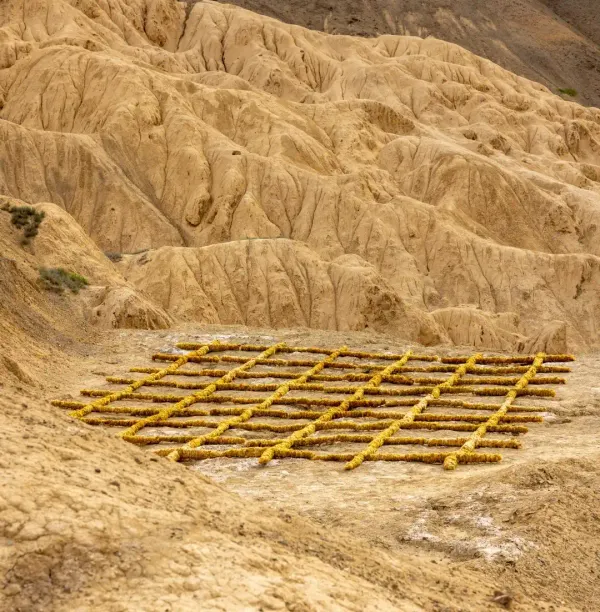 A yellow grid land art installation by Studio Eidola resting on the dry, eroded mountain terrain of Lamayuru for the sa Ladakh Biennale.