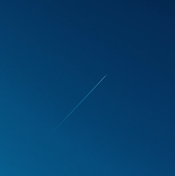A single airplane leaving a thin white contrail across a vast, deep blue minimal sky.