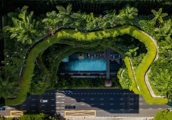 Aerial view of a biophilic building in Singapore with lush green terraces directly contrasting with the adjacent asphalt city road.