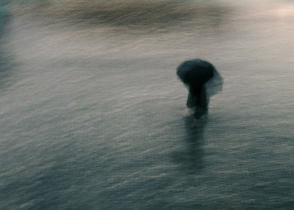 A heavily blurred silhouette of a solitary figure with an umbrella walking in the rain, symbolizing urban isolation and visibility fatigue.
