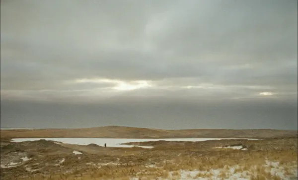 Wide 16mm film still of a winter landscape on Sable Island with naturalist Zoe Lucas in Geographies of Solitude.