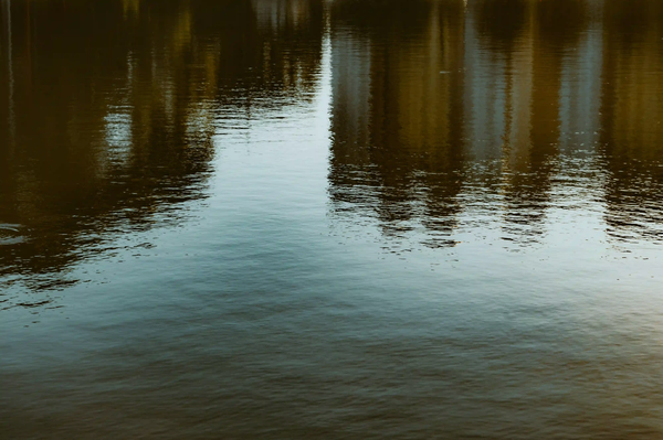Dark reflections of massive concrete buildings on the surface of an urban waterway.
