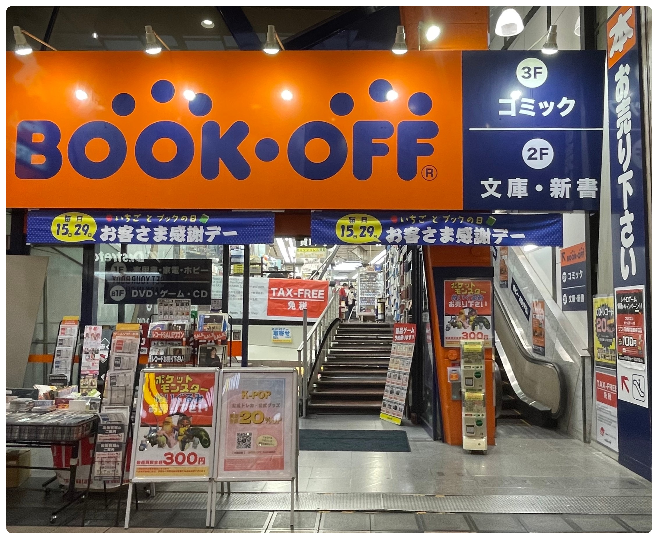 The entrance to the BOOKOFF store in Osaka's Shinsaibashi, with a large orange sign above escalators and racks of secondhand games and books.