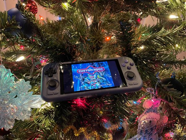 A handheld gaming console sits in a decorated Christmas tree lit with multicolor lights.