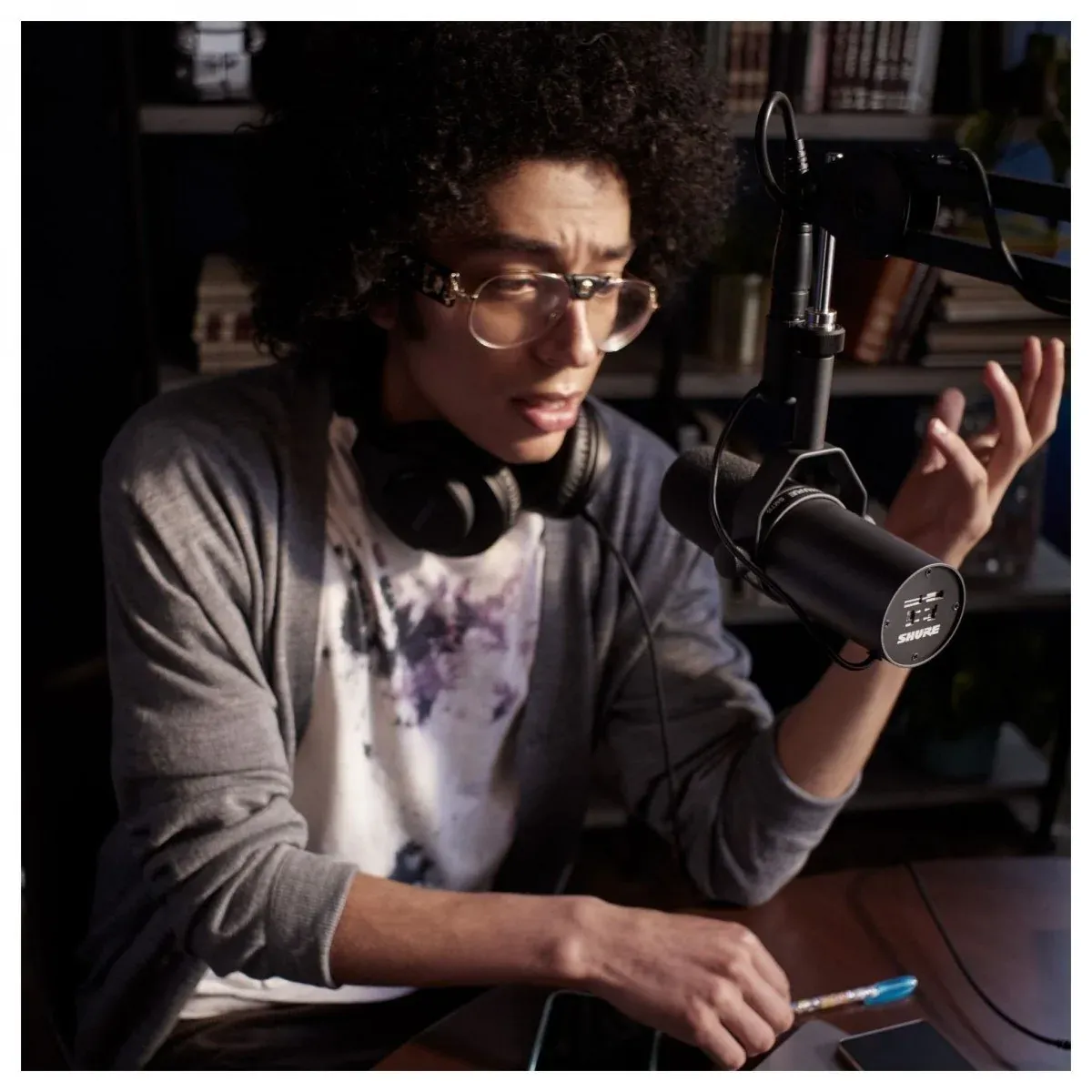 戴眼鏡的男生坐在書房裡,對著裝在懸臂支架上的 Shure SM7B 說話、錄 Podcast