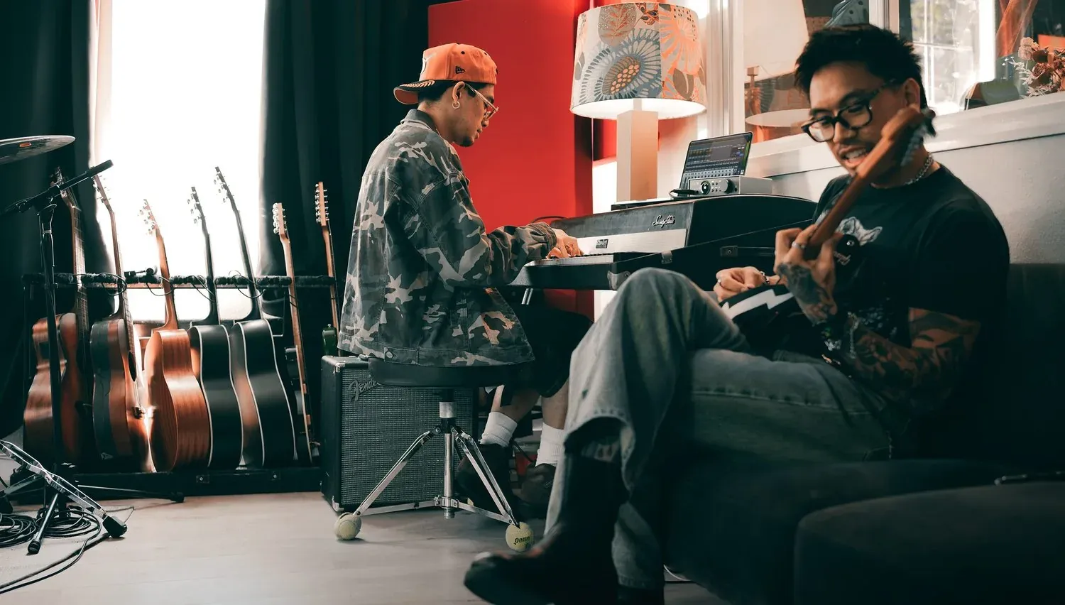 兩位音樂人在家中的錄音角落，一位彈鍵盤、一位抱著電吉他，牆邊架著多把吉他