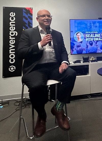 Image: Andrew in the host seat, sitting on a stool with mic in hand.