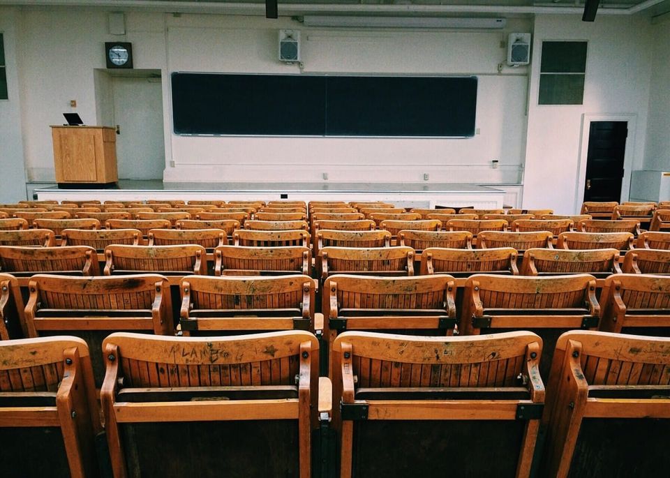 Image of classroom with empty wood chairs facing white board and lecturer podium.