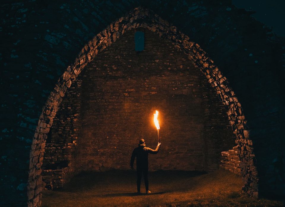 Image: Man in a dark arched bricked hallway lights his path with a torch