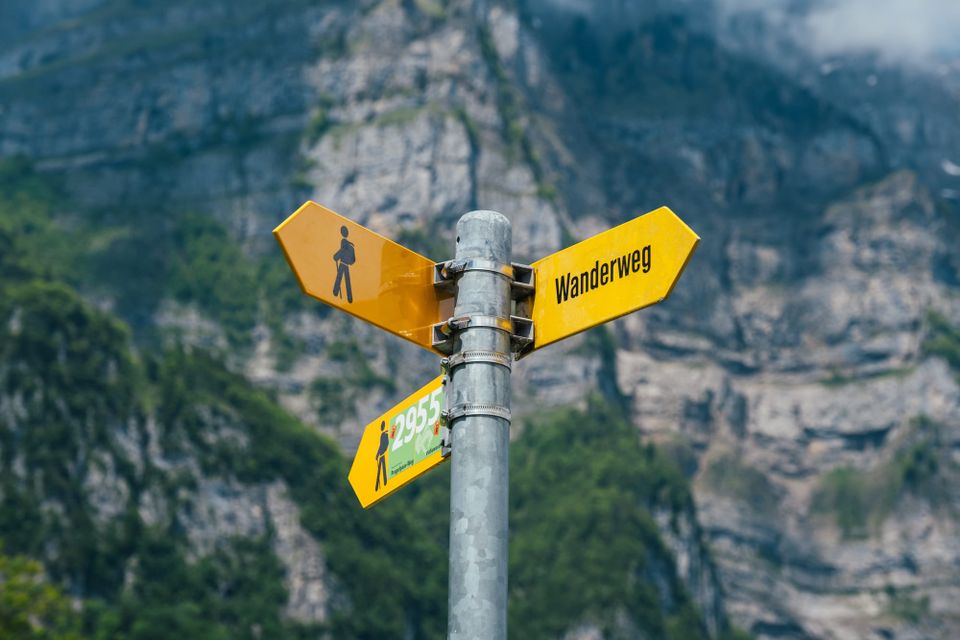 Image: Yellow directional signpost with mountain in the foreground.
