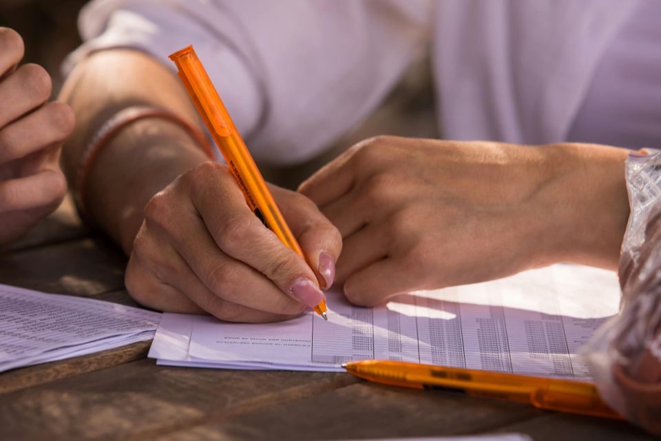 Image: Close up of a pair of hands holding an orange pen looking at a printed spreadsheet.