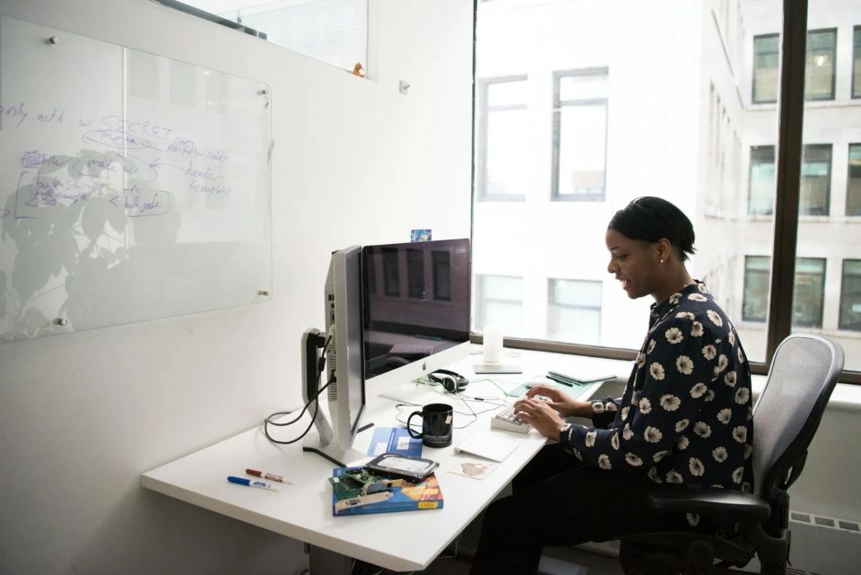 Image: IT analyst in sunflower print blouse works at her desk.
