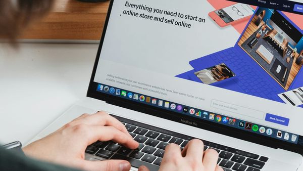 A person sitting at a desk near a window types on a MacBook Pro displaying the Shopify website