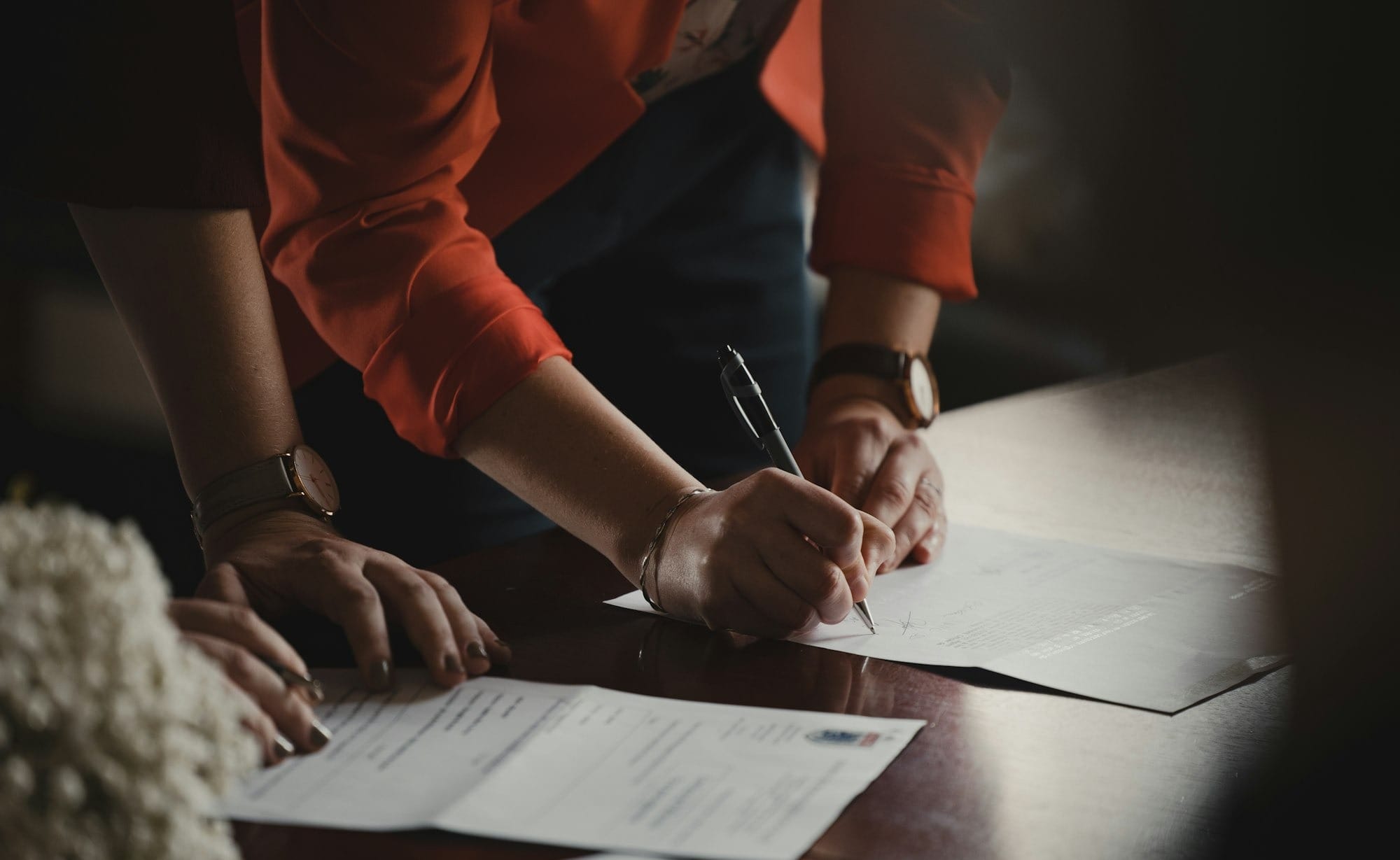 person in orange long sleeve shirt writing on white paper