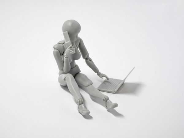 A toy robot sitting at a laptop keyboard
