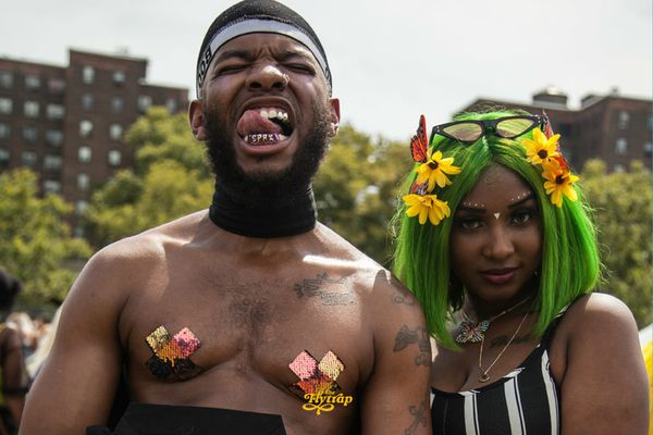 Two Afropunk attendees, a Black man wearing iridescent pasties and a Black woman with green hair and a striped black and white top.