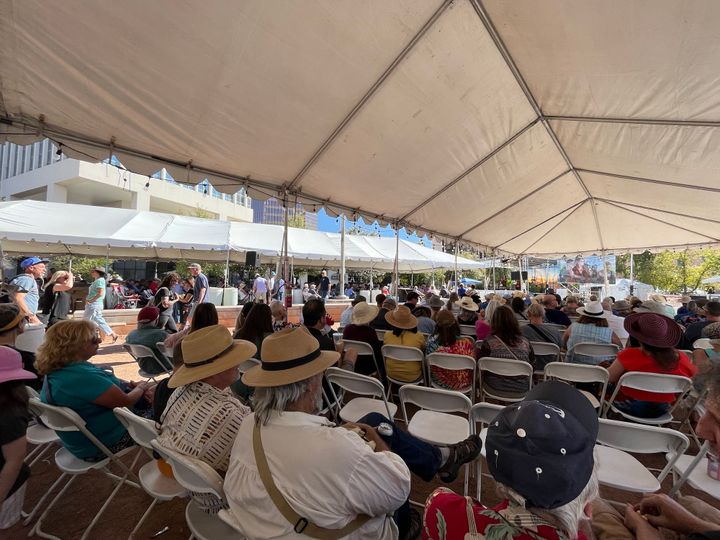 Hundreds of people watching a band on stage from under two large white tents sitting on folding chairs