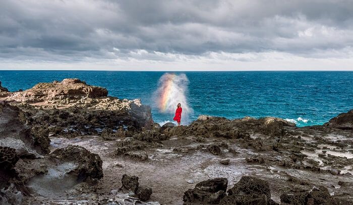 A lady in red stood on rocks infront of the sea
