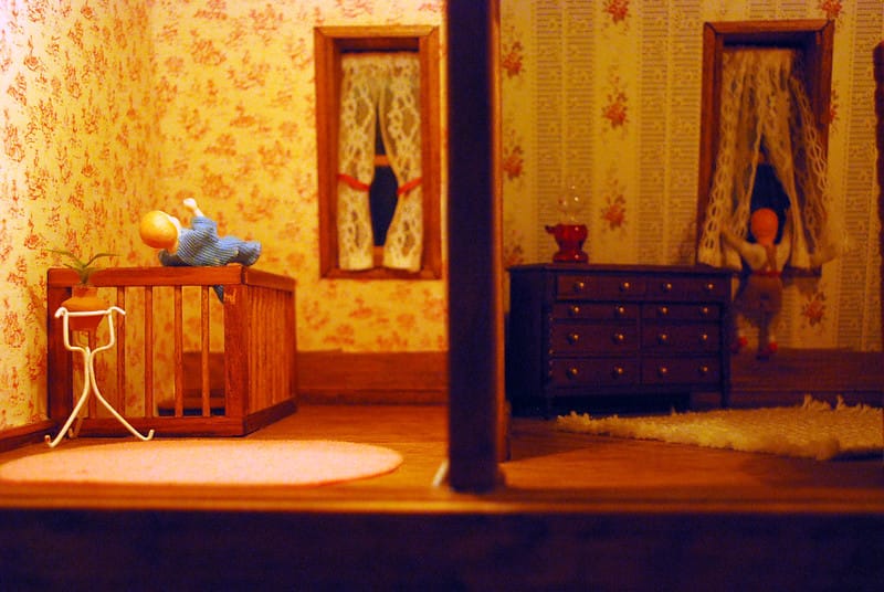 Two rooms in a dollhouse. They have sickly yellow-white wallpaper with complicated patterns. In the one on the left, a baby is perched precariously on the railing of a staircase. In the other, a toddler is opening a window.