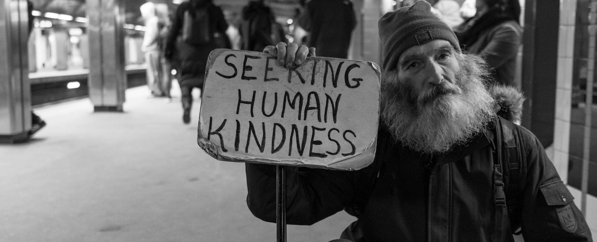 man holding card with seeking human kindness text