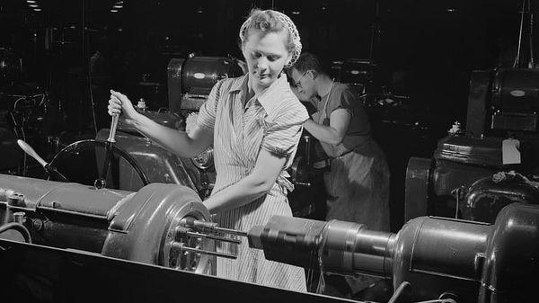 A woman operates a metal lathe in this black and white photo.